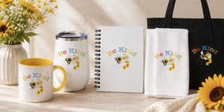 Be Kind Signature Collection featuring a mug, tumbler, journal, and tote bag with cheerful bee and sunflower artwork.