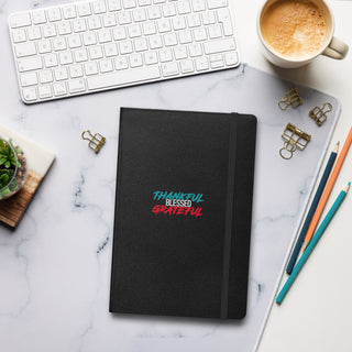 Black Thankful Grateful Blessed Notebook with pencils, paperclips and coffee on desk in the background.